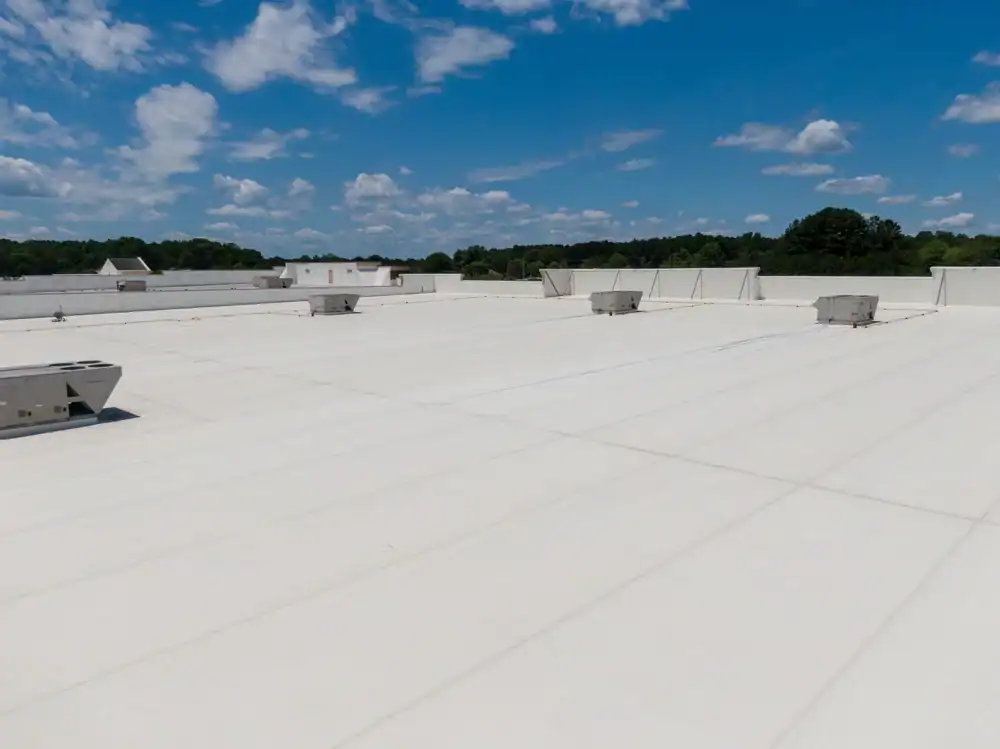 A large flat white commercial rooftop with several HVAC units, maintained by a roofing contractor Southwest Louisiana, under a partly cloudy blue sky and surrounded by trees in the background.
