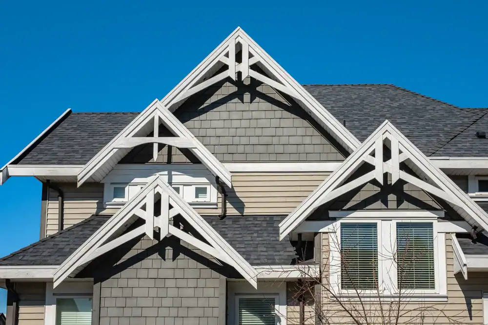 House with multiple peaked gables, gray siding, white trim, and several windows set against a clear blue sky—perfect inspiration for anyone seeking a skilled roofing contractor in Southwest Louisiana or a roofer in Jasper County, TX.